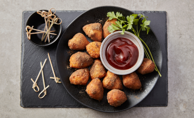 Fried biscuit bites tossed in garam masala then paired with tamarind stirred into ketchup for a simple, tangy dipping sauce. All on black serving platter with side serving skewers.