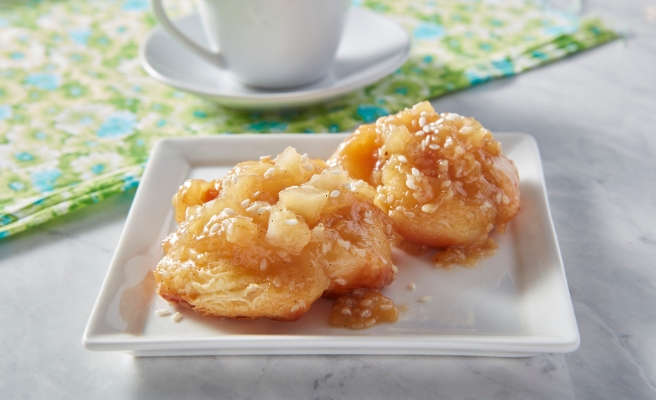 Miso caramel and pear croissant sticky buns with sesame seed garnish all on a white square plate. Green and blue floral fabric in the background with a white teacup and saucer.